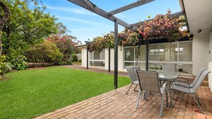 A patio with a table and chairs, a grassy lawn, and a garden with various plants and trees.