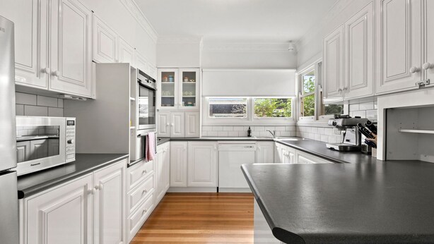 A modern kitchen with white cabinetry, a built-in oven, a microwave, and a coffee machine.