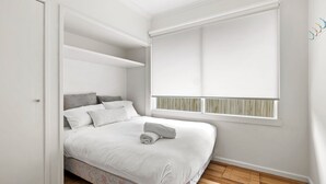 A bedroom with a bed, a window with blinds, and a built-in wardrobe.