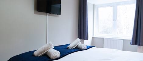 A hotel room with a bed, a flat-screen TV mounted on the wall, and a window with curtains.