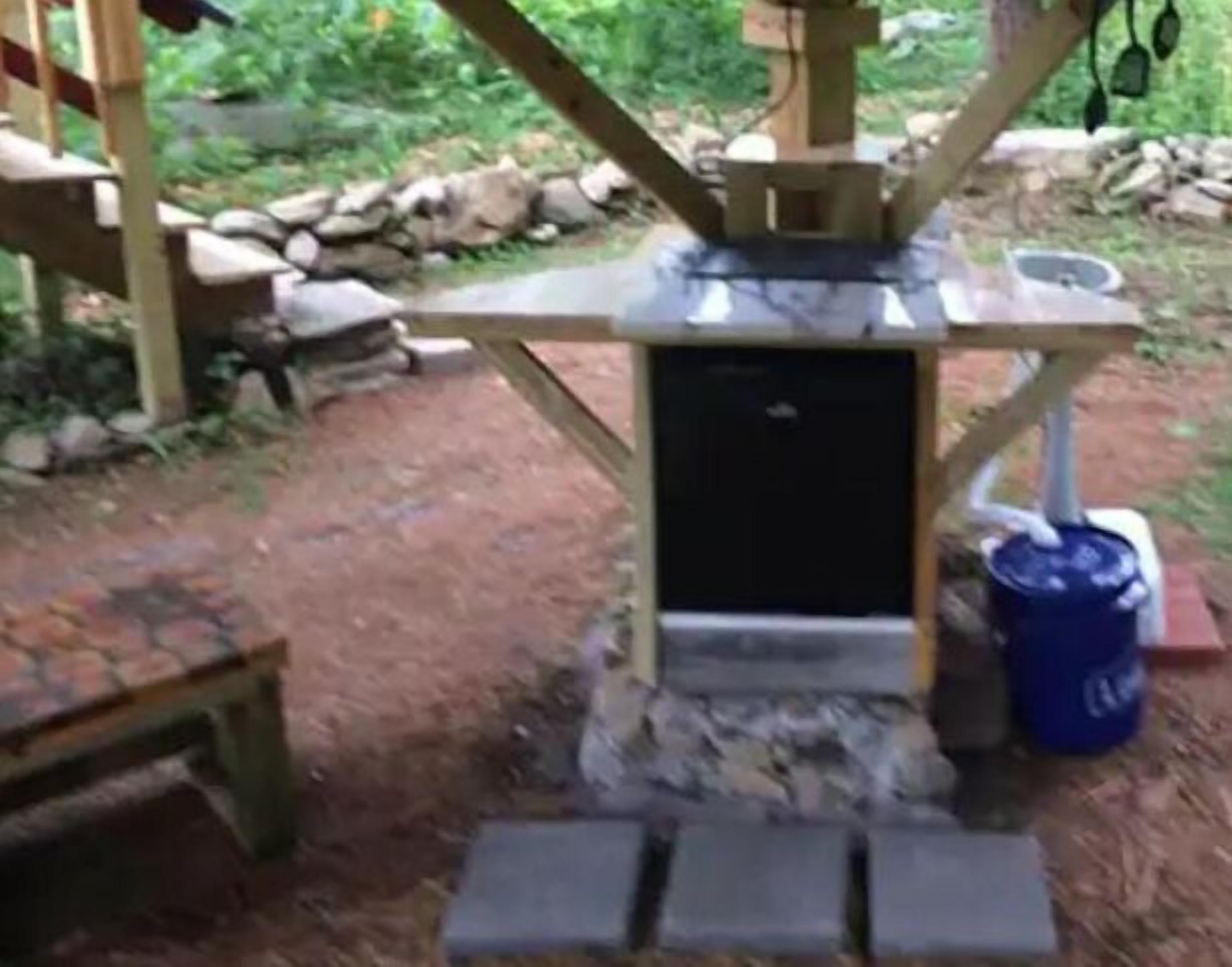 A rustic outdoor setting with a stone structure, a small black cabinet, and a blue barrel.