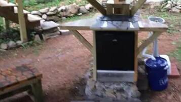 A rustic outdoor setting with a stone structure, a small black cabinet, and a blue barrel.