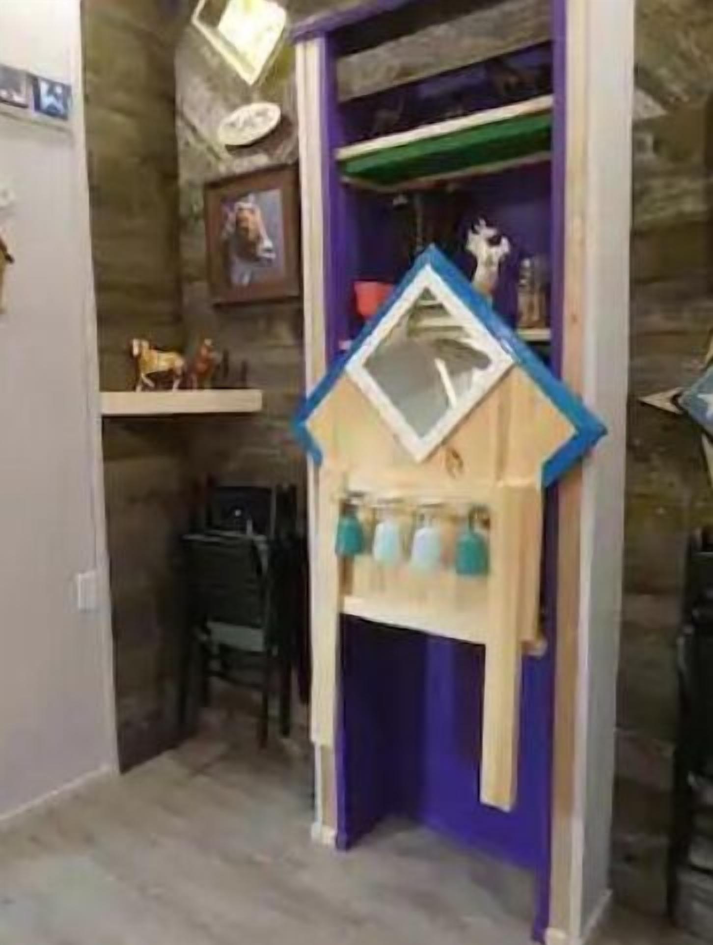 A room with a wooden playhouse featuring a blue roof and a shelf with cups.