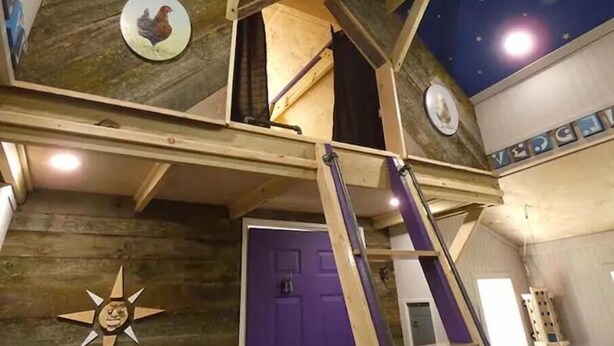 A room with a sloped ceiling, wooden beams, a purple door, and a star decoration on the wall. - The Tree House at Underhill Hollow (Thompson)