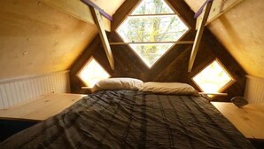 A bedroom with a sloped ceiling, wooden walls, and two skylights. - The Tree House at Underhill Hollow (Thompson)