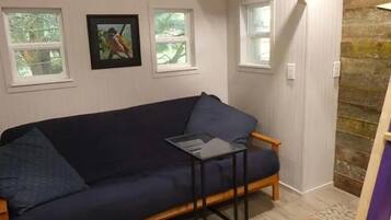 A room with a dark blue sofa, a small black table, and a patterned rug. There are three windows with white frames, and a picture is hanging on the wall.