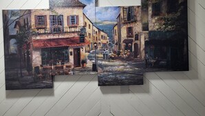 Una obra de arte en varios paneles que muestra una escena callejera con edificios, un café y una cafetería.