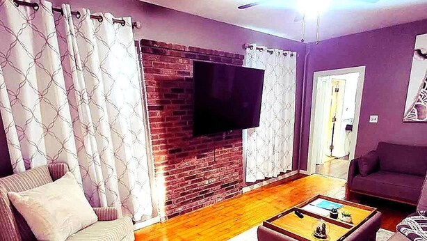 Una sala de estar con chimenea de ladrillo, un televisor de pantalla plana montado en la pared, una mesa de centro de madera y dos sofás.