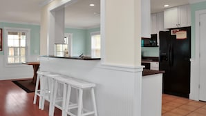A kitchen with white cabinets, a black refrigerator, and a bar area with white stools. - Cape Dreamin' (Port St. Joe)
