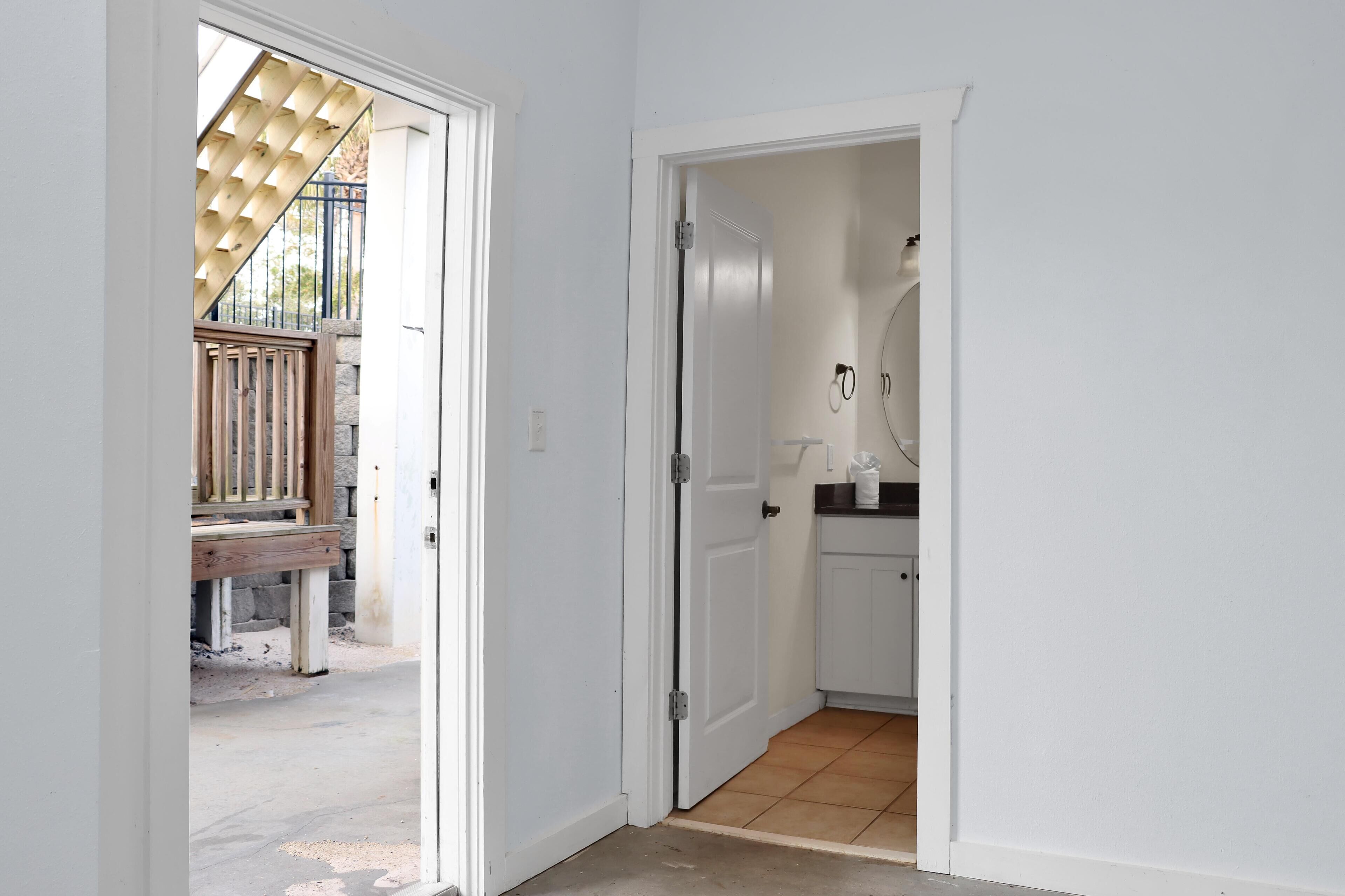 A hallway with a wooden bench outside, a white door leading to a bathroom, and a kitchen area visible through the door.
