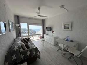 Ein modernes Wohnzimmer mit einer Couch, einem Schreibtisch, einem Fernseher und einem Balkon mit Blick.
