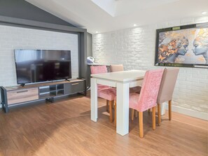 A modern living room with a flat-screen TV, a dining table with pink chairs, and a white brick wall with a decorative painting. - Taksim By Aydın Suite Hotel (Istanbul)