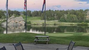 Une terrasse extérieure dotée d’un foyer, de chaises et offrant une vue sur un terrain de golf et un lac.