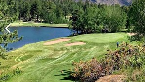 Un parcours de golf avec un étang, entouré d’arbres et de montagnes.