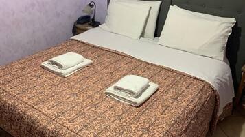 A neatly made bed with a patterned bedspread and two folded towels, a nightstand with a lamp, and a wall-mounted picture.
