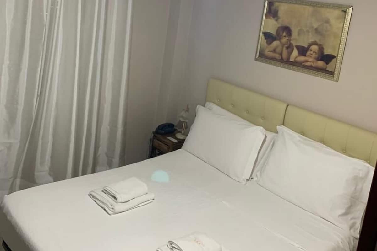 A neatly made bed with white linens and towels, a bedside table with a lamp, and a painting on the wall.