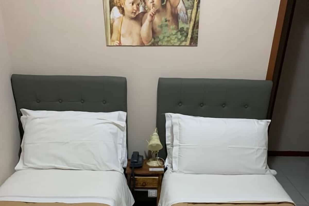 A double bed room with two beds, each with a brown quilted bedspread and white pillows. There is a nightstand with a lamp and a phone between the beds.