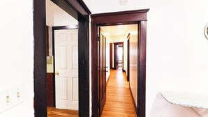 A hallway with wooden flooring, a white door, and a wall-mounted light fixture. - Best in Buffalo Entire First Floor up to 6 guests (Buffalo)