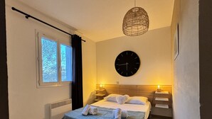 Une chambre à coucher bien rangée, avec un lit, des lampes de chevet, une horloge murale et une fenêtre avec des rideaux.