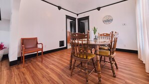 Un coin repas avec une table et des chaises en bois, une horloge au mur et une porte visible au fond.