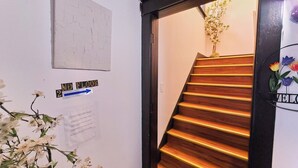 Un escalier avec des marches en bois et une structure sombre, menant à une pièce dont un mur est blanc et où se trouve un petit arrangement floral.