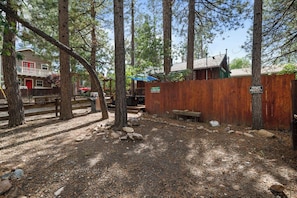 Un espace boisé, délimité par une clôture en bois, avec un banc et un bâtiment dont la porte est rouge.