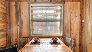 Un interior de madera con una mesa dispuesta para dos personas, una ventana con persianas y un radiador.