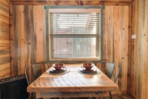Un intérieur en bois avec une table dressée pour deux personnes, une fenêtre avec des stores et un radiateur.