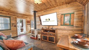 Un interior de madera con chimenea, un televisor montado en la pared y una mesa de comedor con cuencos.