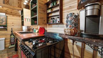 Une cuisine avec des murs en bois, une cuisinière à gaz, un évier et des étagères remplies de divers objets.