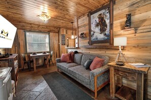 L’intérieur chaleureux d’un chalet avec un plafond en bois, un coin repas comprenant une table et des chaises, un canapé avec des coussins et un tableau accroché au mur.