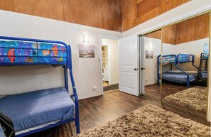 A room with bunk beds, a mirror, and a door leading to another room.