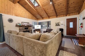 Un salon chaleureux avec un grand canapé d’angle, une cheminée en pierre et un plafond en bois.