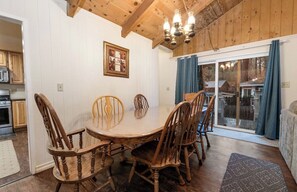A dining area with a wooden table and chairs, a chandelier, and a view through a glass door.