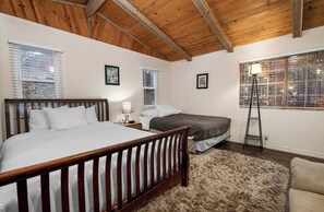 Une chambre avec un plafond en bois, deux lits, une lampe sur pied et une grande fenêtre avec des stores.
