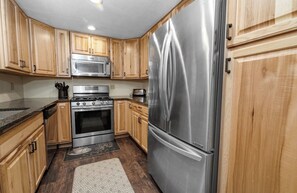 Une cuisine avec des meubles en bois, des appareils électroménagers en acier inoxydable et un tapis à motifs.