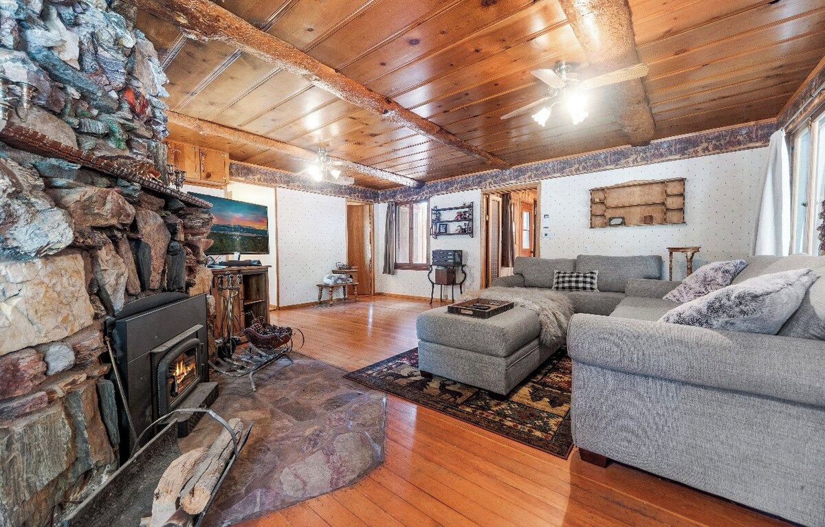 A cozy living room with a stone fireplace, wooden ceiling, and a grey sofa.