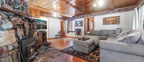 Una sala de estar acogedora con chimenea de piedra, techo de madera y sofá gris.