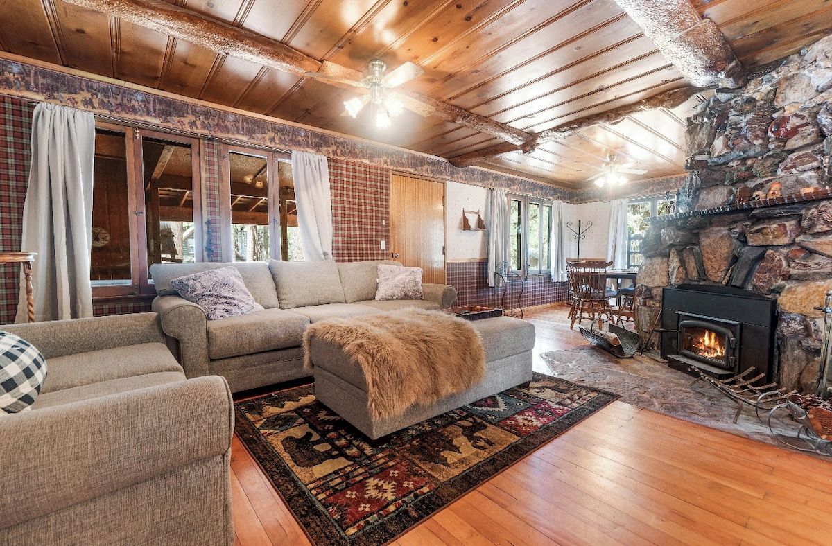 A cozy living room with a stone fireplace, wooden ceiling beams, and a large sectional sofa.
