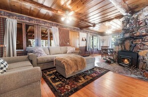 A cozy living room with a stone fireplace, wooden ceiling beams, and a large sectional sofa.