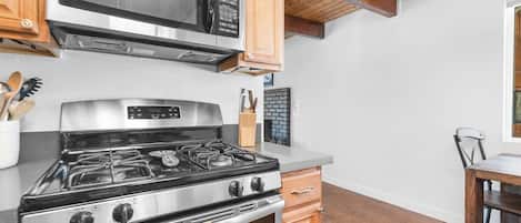 A kitchen with a stainless steel stove, a microwave, wooden cabinets, and a brick wall backsplash.