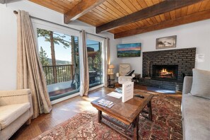 A living room with a fireplace, a sofa, a coffee table, and a view through a glass door. - Wondrous Juniper House (Big Bear Lake)