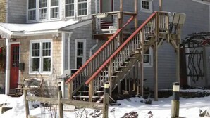 Una casa a due piani con una porta rossa, finestre bianche e una scala in legno.