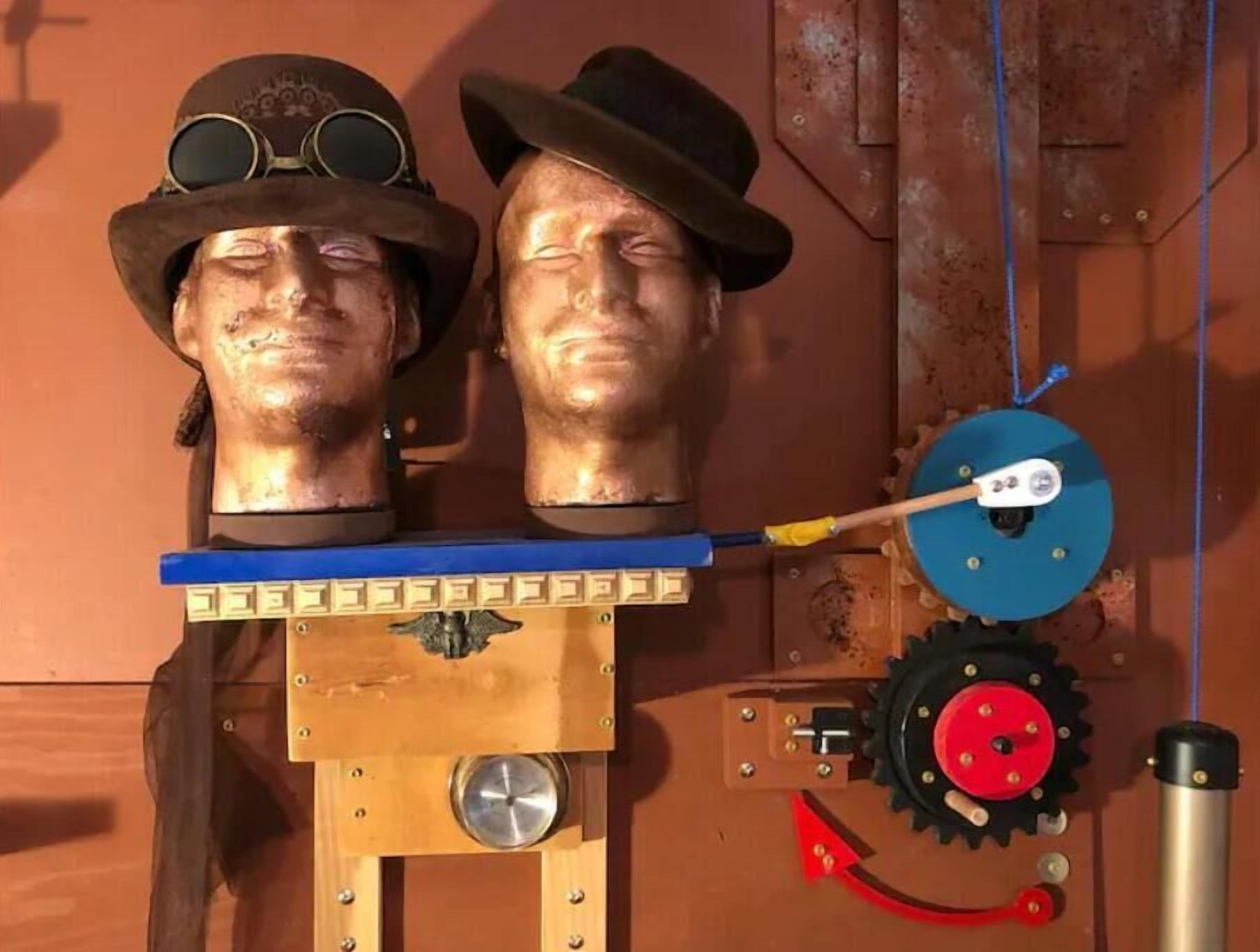 Two head sculptures mounted on a wooden structure with gears and a pulley system.