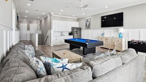 A modern living room with a pool table, grey sofa, and a flat-screen TV.