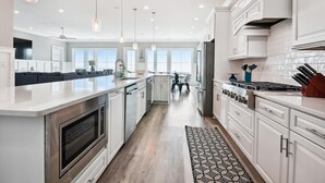 A modern kitchen with white cabinetry, a central island, stainless steel appliances, pendant lighting, and a view to the dining area.