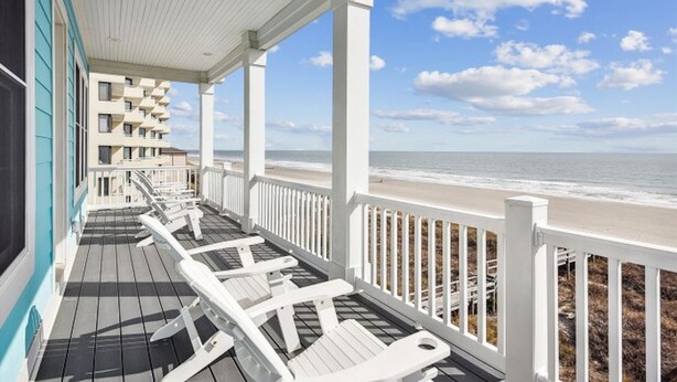 A covered deck with white railings overlooking a beach.