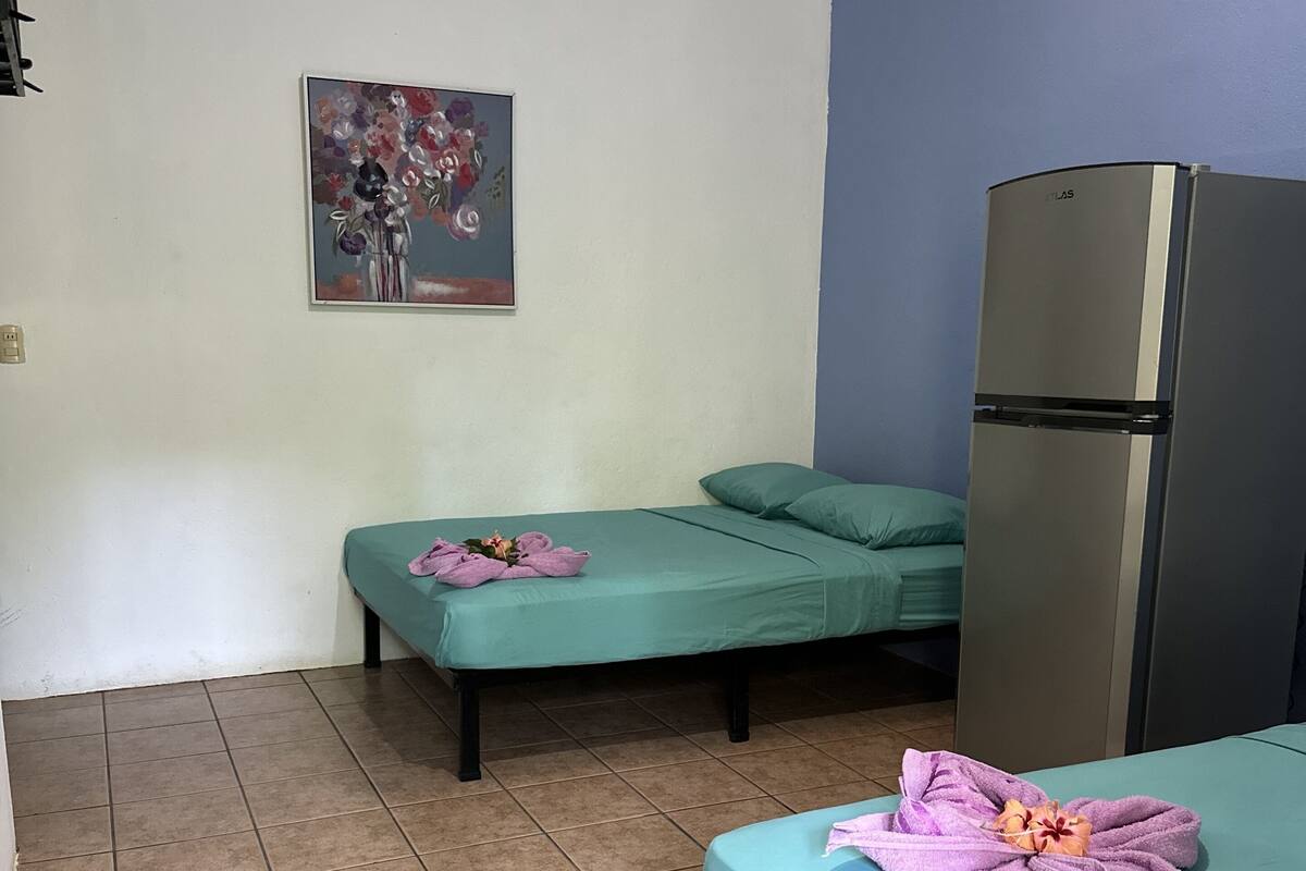 A room with two beds, a refrigerator, and a painting on the wall.
