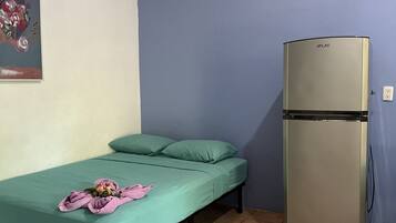 Una habitación pequeña con una cama, un colchón verde, una toalla rosa y un refrigerador.