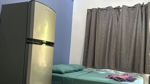 A room with a bed, a small table, a refrigerator, and a window with curtains. - Wide Mouth Frog Conchal (Cabo Velas)